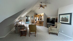 Un loft espacioso con techo alto, ventilador de techo, comedor, cocina, sala de estar con televisor y un cuadro en la pared.