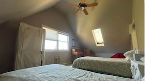 Un dormitorio con dos camas, ventilador de techo, ventana y radiador.