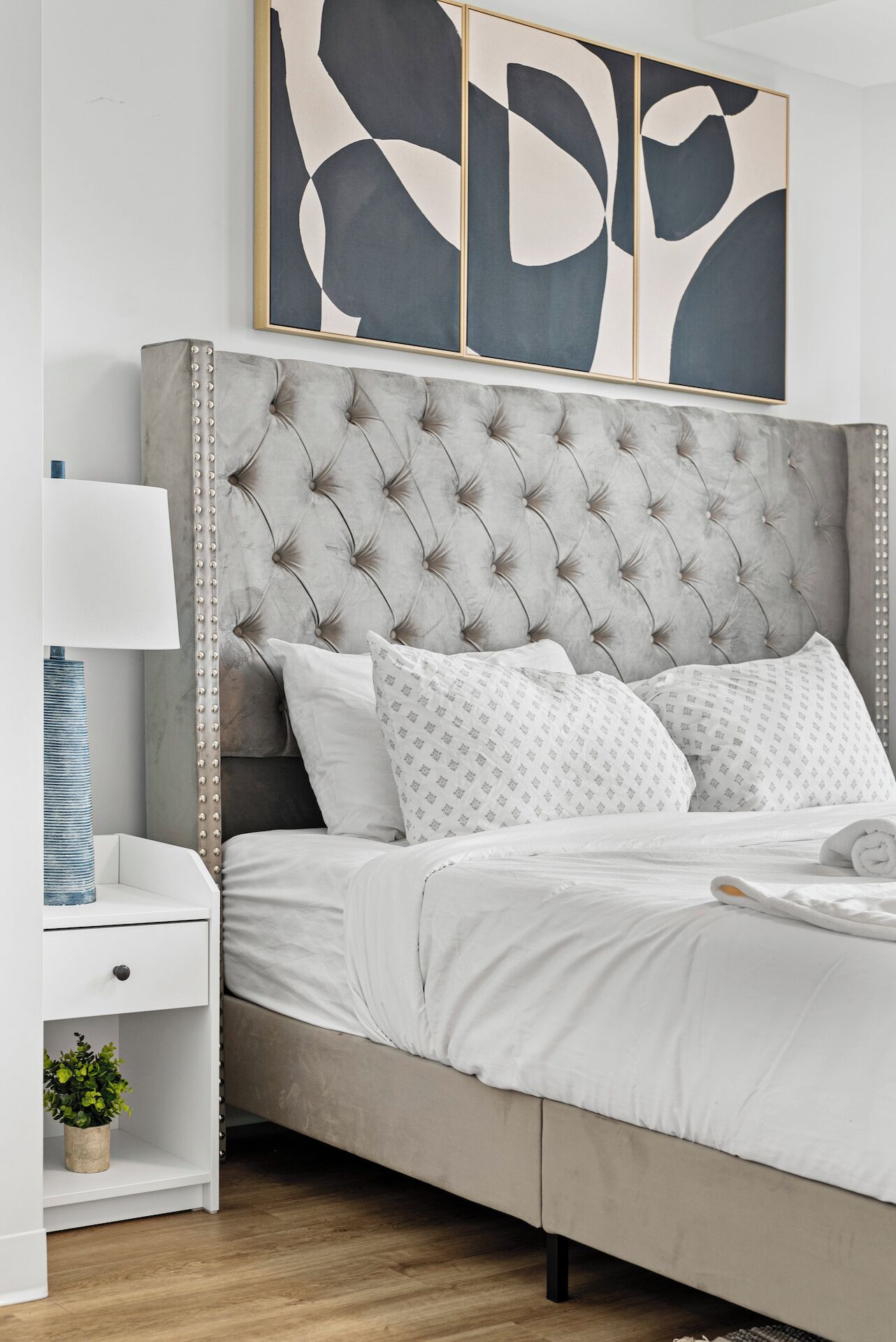 A bedroom with a tufted headboard, white bedding, and a bedside table with a lamp.