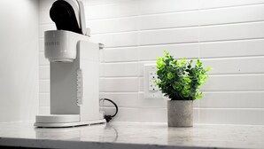 Una cafetera blanca sobre una encimera de cocina, junto a una planta en maceta.