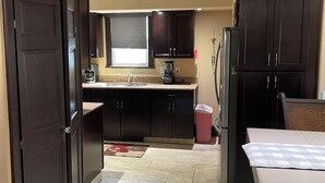 A kitchen with dark wooden cabinets, a countertop, a window with blinds, a coffee maker, and a trash bin. - 3-bedroom house in tranquil Harvey with WiFi, AC. Relax and unwind (Harvey)