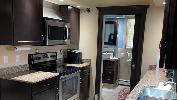A modern kitchen with dark cabinetry, granite countertops, stainless steel appliances, and a visible island with a sink. - 3-bedroom house in tranquil Harvey with WiFi, AC. Relax and unwind (Harvey)