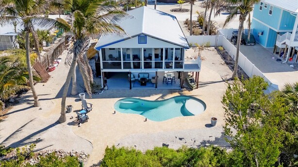 Una propiedad frente a la playa con piscina, palmeras y una casa grande con balcón.