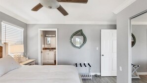 Un dormitorio con cama, ventilador de techo, baño con espejo y puerta que da a otra habitación.