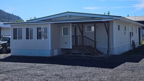 A single-story mobile home with a porch, a front door, and a staircase leading to the entrance. - The Queen 2 Bedroom Apartment D (Craig)