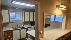 A compact kitchen with wooden cabinets, a built-in dishwasher, a coffee maker, and a window with a view of a snowy landscape. - The Queen 2 Bedroom Apartment D (Craig)