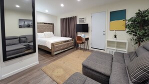 A modern hotel room with a bed, a sofa, a desk, and a television.