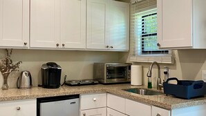 A kitchen with white cabinets, a dishwasher, a coffee maker, a toaster, and a window with blinds.