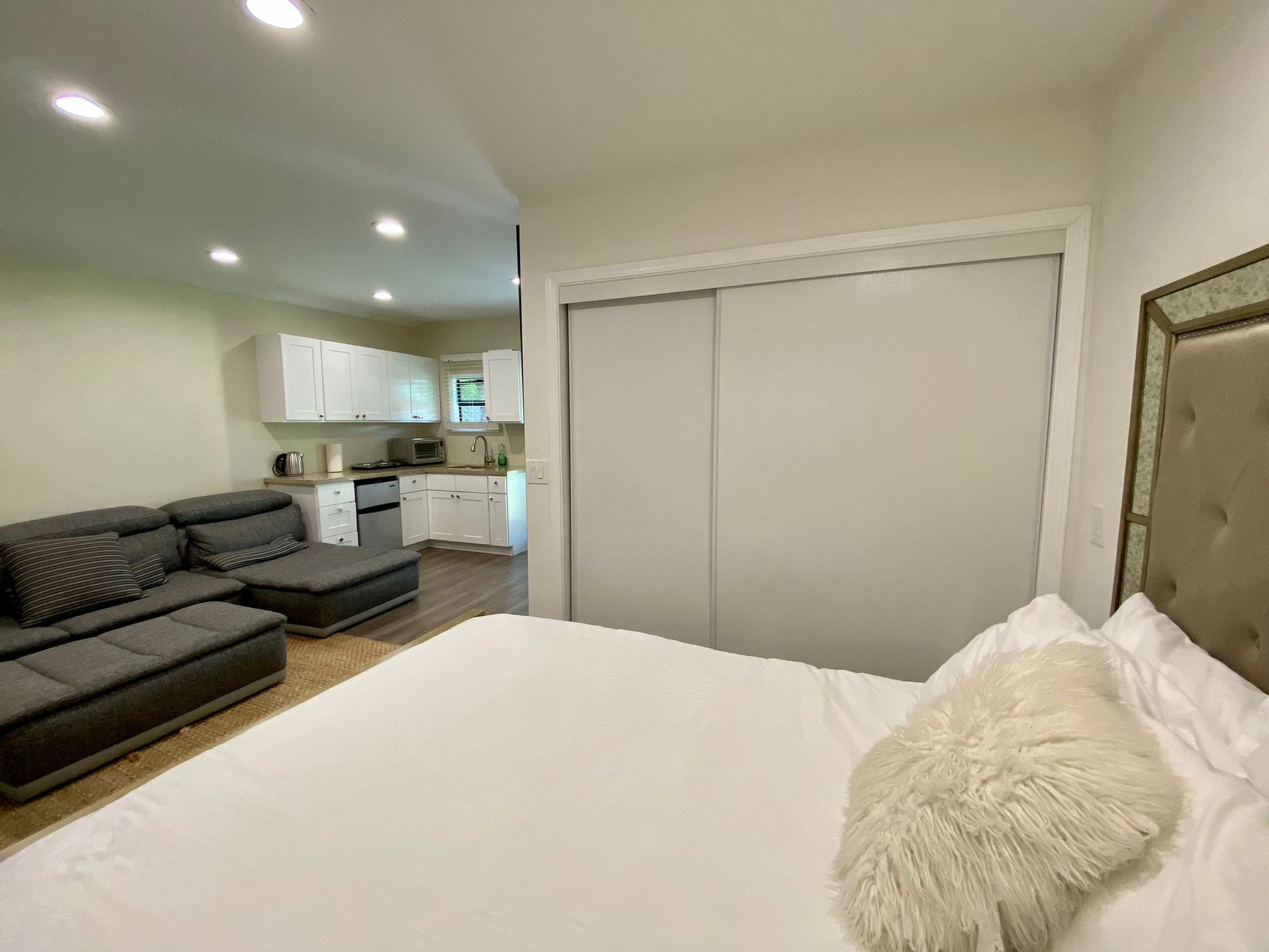Ein Schlafzimmer mit Bett, einem grauen Sofa und einer Küche im Hintergrund.