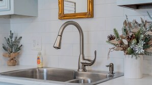 A kitchen with a stainless steel sink, a gold-framed mirror, and a decorative plant. - Charming Creekside Cottage [] Near Downtown, OSU & Airport (Gahanna)