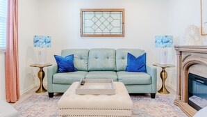 A living room with a light green sofa, two blue pillows, a tray on an ottoman, and a fireplace. - Charming Creekside Cottage [] Near Downtown, OSU & Airport (Gahanna)