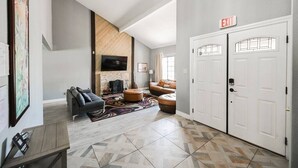 A spacious living area with a fireplace, a sofa, and a coffee table. There are two white doors with an exit sign above them. - The Nuevo Luxe Villa (Henderson)