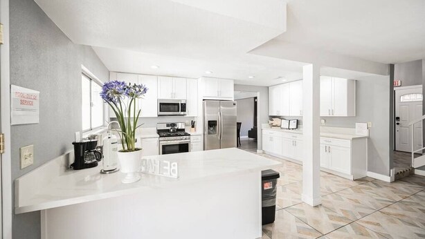 A modern kitchen with white cabinetry, a central island, and a sign indicating a pool exit service area. - The Nuevo Luxe Villa (Henderson)