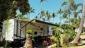 A recreational vehicle (RV) parked in a tropical setting with palm trees and greenery.