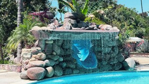A pool with a rock waterfall feature surrounded by tropical plants.