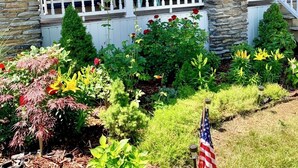 A house with a stone facade, white railings, and hanging flower baskets with American flags.