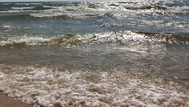 A beach with waves crashing onto the shore under a clear sky.