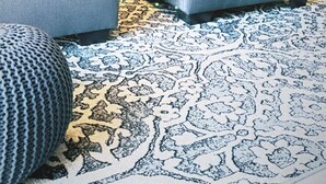Ein modernes Wohnzimmer mit einem Ecksofa, einem Hocker und einem gemusterten Teppich.