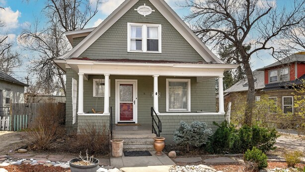 A two-story house with a front porch, a red door, and a small front yard with a potted plant and a stone pathway.