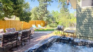 A hot tub with a wooden deck, outdoor furniture, and a wooden fence in the background.