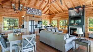 A spacious cabin interior with a dining area, sofa, fireplace, and kitchen.
