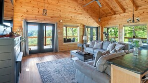 A cozy cabin interior with a wooden ceiling, a sofa, a coffee table, and a view of the outdoors.