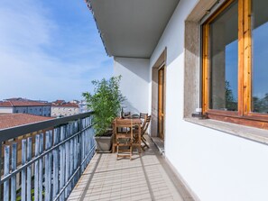 A balcony with a wooden table and chairs, a potted plant, and a view of buildings in the background.