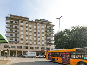 A multi-story building with a central entrance, a parked white truck, and an orange bus.