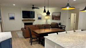 Une cuisine moderne avec un plan de travail en marbre, une table à manger avec des chaises, un canapé en cuir et des luminaires suspendus.