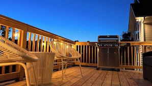 Une terrasse en bois avec un barbecue et des chaises en osier.