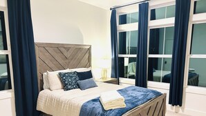 Un lit bien fait, avec une tête de lit en bois, une couverture bleue et une serviette blanche pliée.