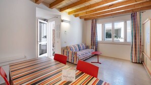 Une pièce avec une table à rayures, des chaises rouges, un canapé à rayures, des poutres en bois, une fenêtre avec des rideaux et une porte donnant sur une autre pièce.