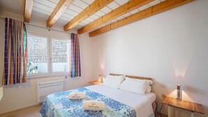 Une chambre à coucher avec un lit, une fenêtre avec des rideaux, une table de chevet avec une lampe et un radiateur.