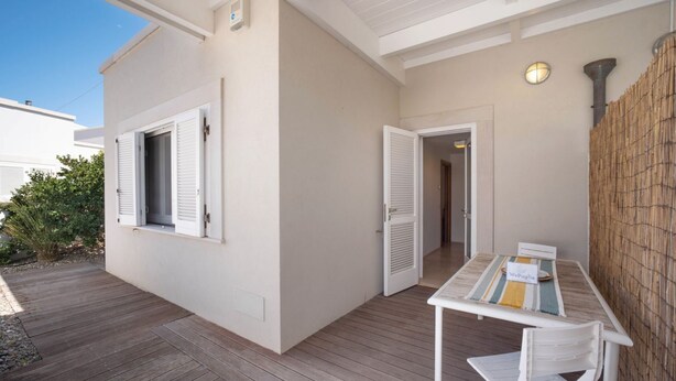 Un patio couvert avec une table et des chaises, un mur en bambou et une porte donnant sur un espace intérieur.