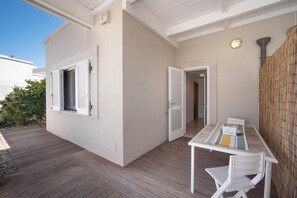 Un patio couvert avec une table et des chaises, un mur en bambou et une porte donnant sur un espace intérieur.