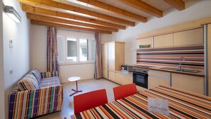 Une cuisine moderne avec des meubles rayés, un coin repas avec une table rayée, un canapé recouvert d’un tissu rayé aux couleurs vives, et une petite table ronde.