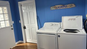 A laundry room with a white washer and dryer, a blue wall, and a door with a window. - Charming 4-bedroom house just a Short walk to Scarborough Beach (Narragansett)