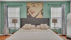 A bedroom with a bed, two bedside tables, a headboard, and a wall painting.