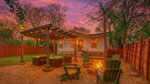 A covered outdoor seating area with Adirondack chairs, a fire pit, and a pergola.