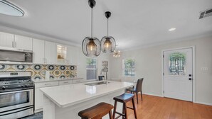 A modern kitchen with white cabinetry, a large island, two pendant lights, and a stainless steel oven.