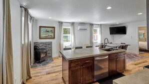 A modern kitchen with a central island, built-in cabinets, and a stone fireplace. - Cozy Forest Cabin, Hot Tub, King beds, AC, Fast Wi-fi, Waterfront, Pet Friendly (Rhododendron)