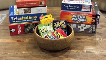 Una mesa de madera con varios juegos de mesa y rompecabezas, incluyendo 'Autumn in the Neighborhood', 'Telestrations', 'Wits & Waggers' y 'UNO'.