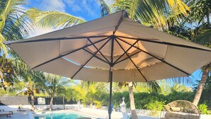 Ein Poolbereich mit rundem Tisch, vier Stühlen, einem Sonnenschirm und einem Schaukelstuhl.