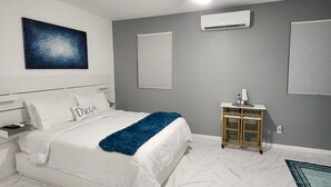 Ein Schlafzimmer mit einem Bett, einem Deckenventilator, einer Klimaanlage, einem Nachttisch mit Lampe sowie einem an der Wand befestigten Kunstwerk.