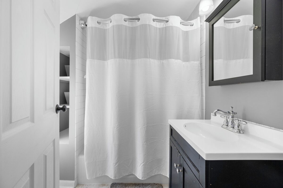 A bathroom with a white shower curtain, a white sink, and a dark cabinet.