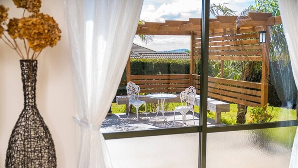 A patio with a wooden pergola, white chairs, and a small table. - Elevated Family Sized Guest-house with Beautiful Views (Auckland)