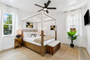 Un dormitorio con una cama con dosel, un ventilador de techo, una planta en maceta y obras de arte en las paredes.