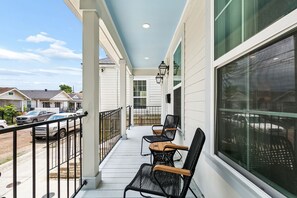 A covered porch with outdoor seating, a view of the street, and a building with large windows.