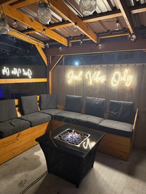 A cozy seating area with a neon sign reading "Good Vibes Only" and a fire pit table. - Entire Home in St. Roch (New Orleans)