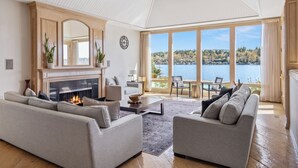 A spacious living room with a fireplace, two sofas, a coffee table, and a large window overlooking a lake. - Stunning Waterfront Mansion w Pool n Hottub (Mercer Island)